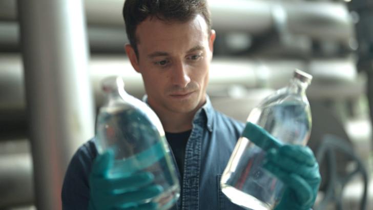 Hugo Clément tient dans chaque main (munie de gant) deux bouteilles